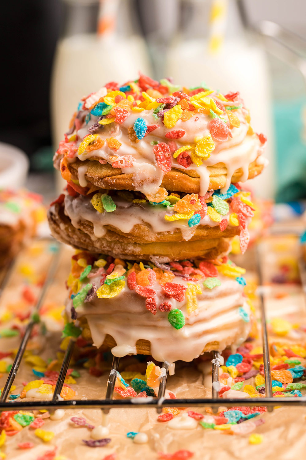 three air fryer fruity pebbles donuts stacked on a wire rack with milk in the background.