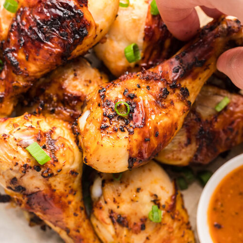 air fryer chicken drumsticks with a dip on the side and scallions on top.