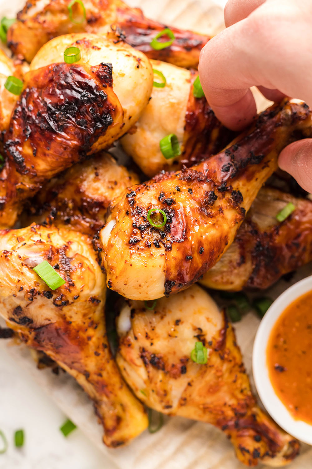 air fryer chicken drumsticks with a dip on the side and scallions on top.