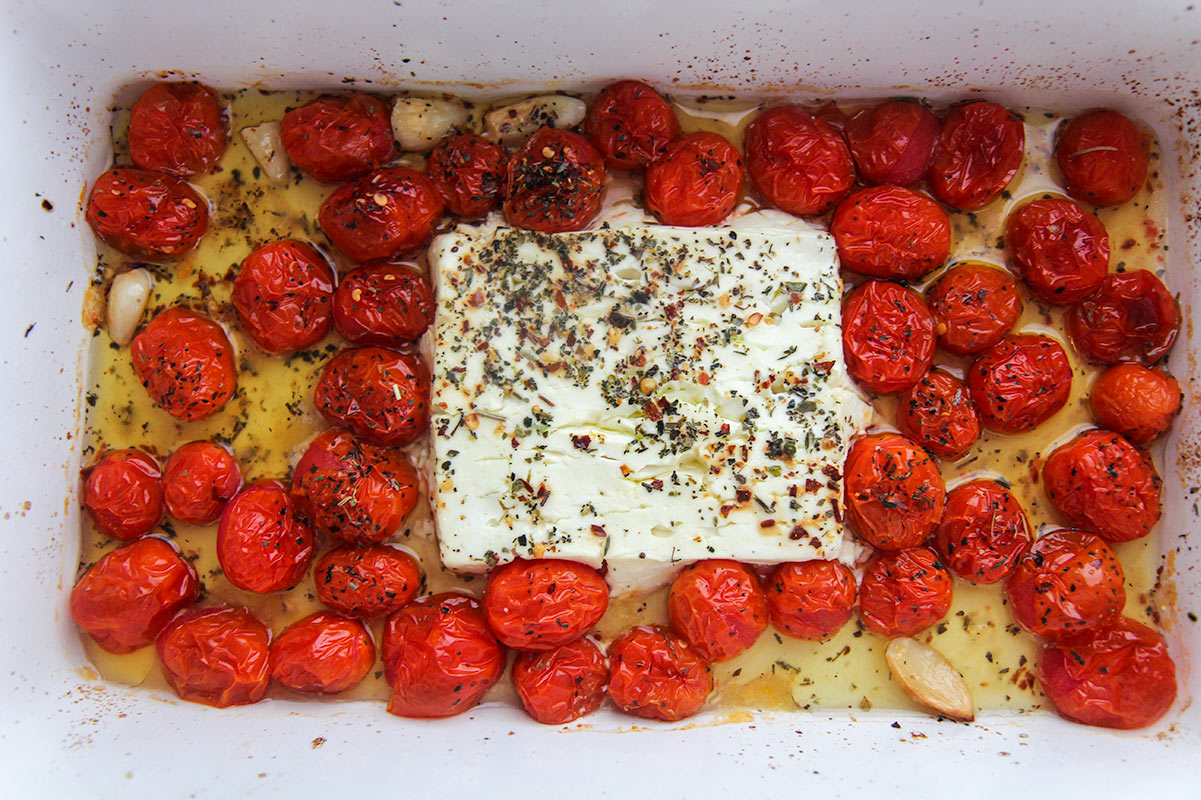 a block of feta cheese, olive oil, Italian seasoning, and cherry tomatoes in a white baking dish.
