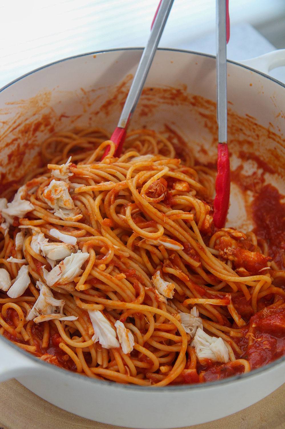 spicy crab bucatini in a white pot with red tongs.