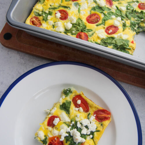 a slice of spinach and goat cheese frittata on a white and blue plate with a 9x13 frittata in the background.