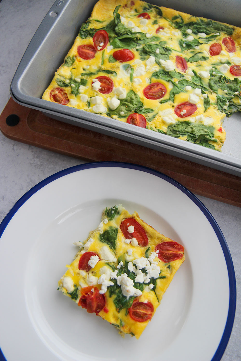 a slice of spinach and goat cheese frittata on a white and blue plate with a 9x13 frittata in the background.