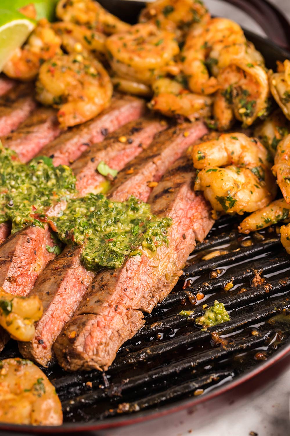 slices of steak with chimichurri on top and shrimp on the side. 