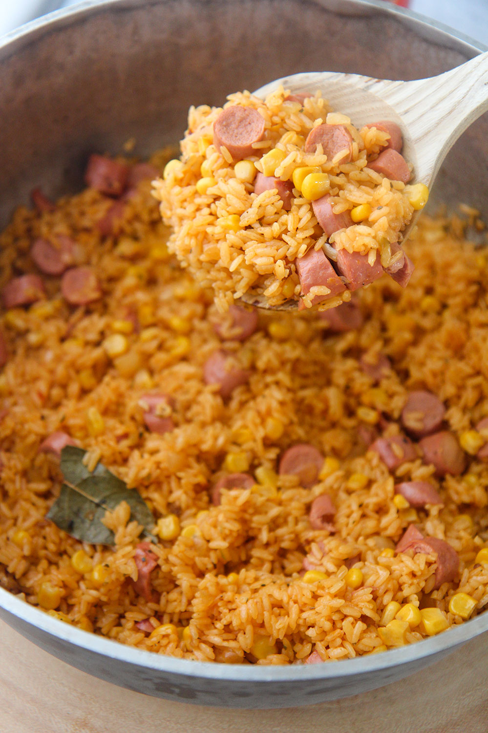 a wooden spoon filled with arroz con salchichas.