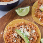 chicken tinga tostadas on a wooden board with lime wedges on the side.