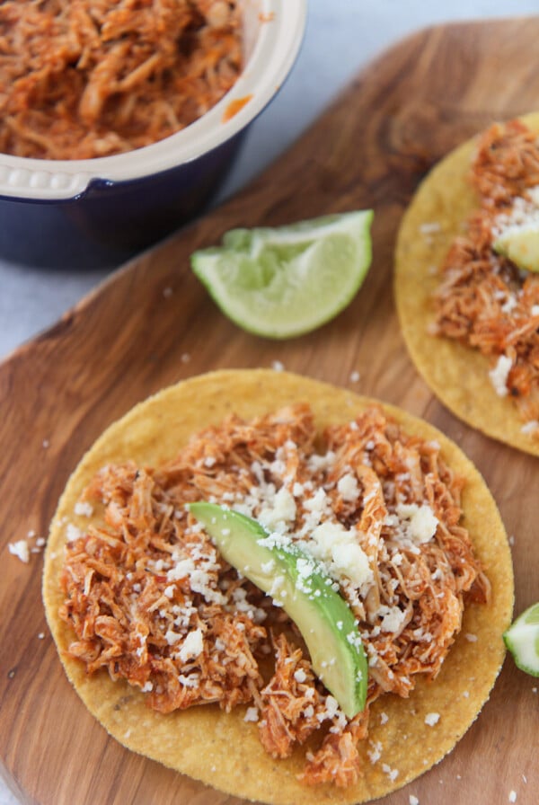 chicken tinga tostadas on a wooden board with lime wedges on the side.
