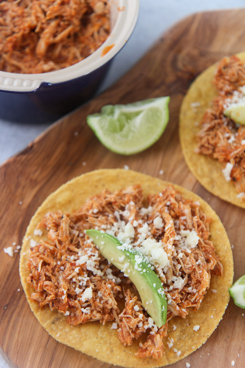 chicken tinga tostadas on a wooden board with lime wedges on the side. 