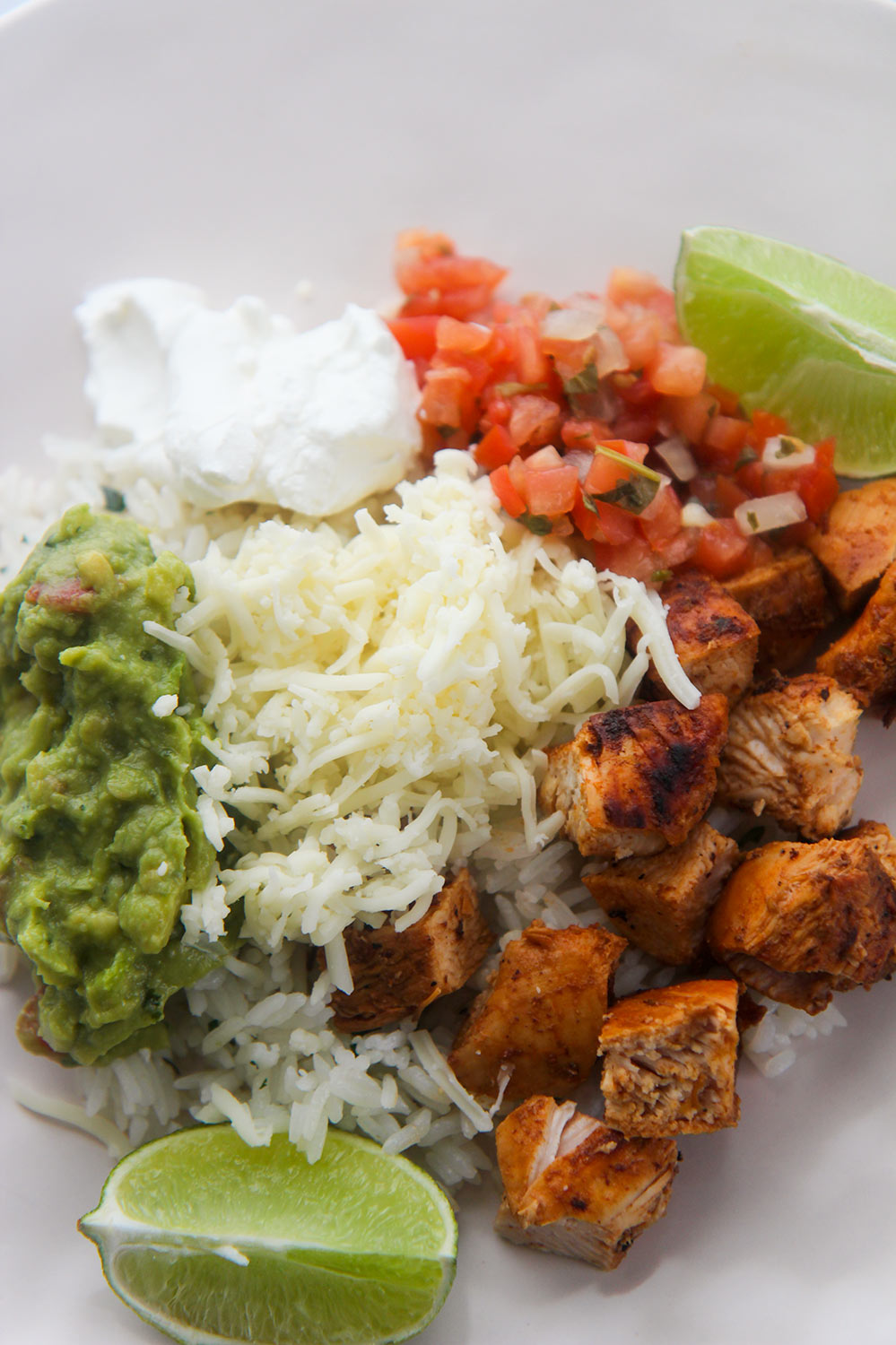 guacamole, cheese, pico de gallo, chicken, sour cream, and lime wedges on a plate. 