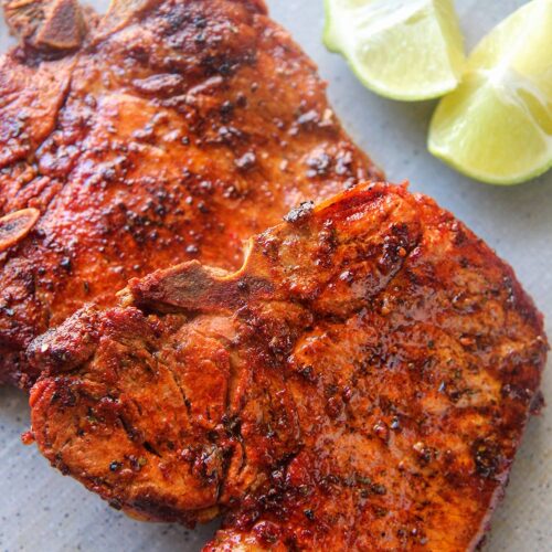 two chuletas fritas on a gray plate with two lime wedges.