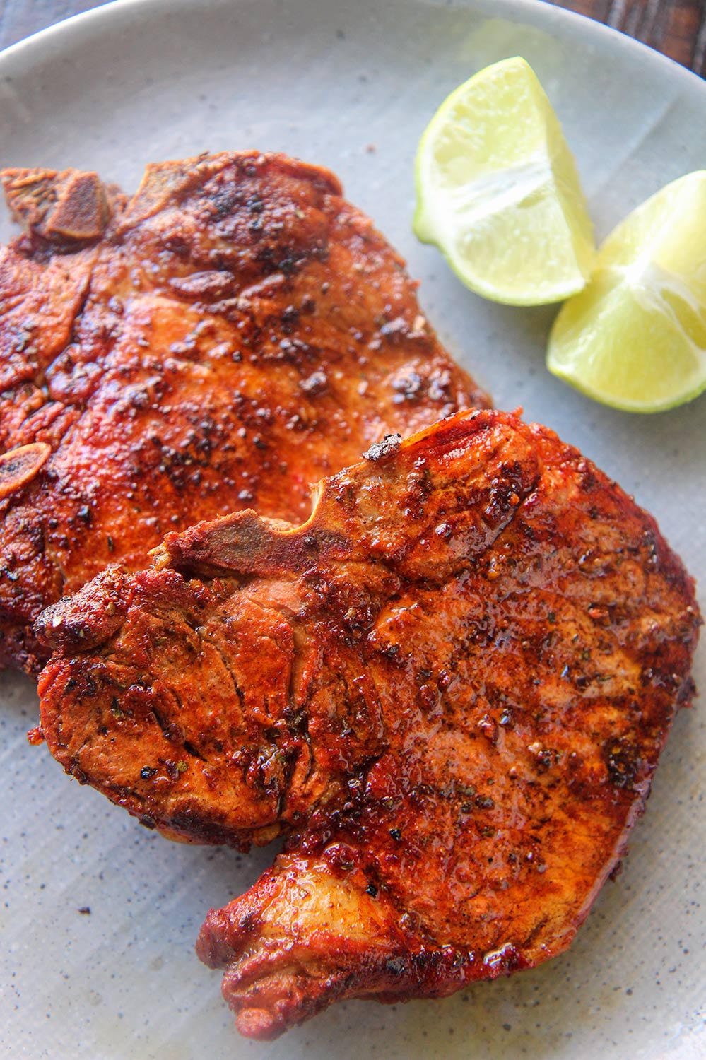 two chuletas fritas on a gray plate with two lime wedges. 