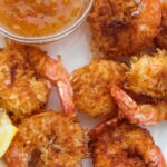 six fried coconut shrimp with orange sauce and lemon wedges on the side.