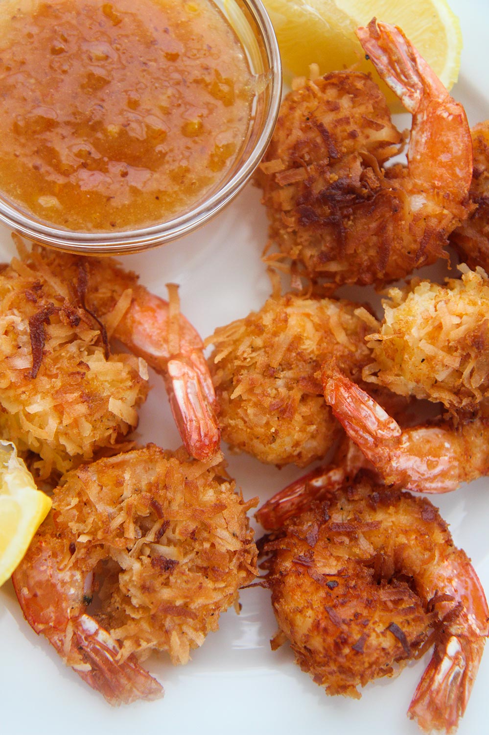 six fried coconut shrimp with orange sauce and lemon wedges on the side.