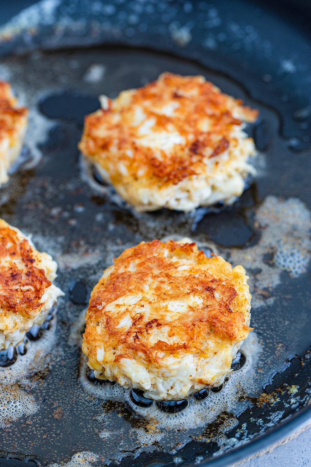 crab cakes frying in a skillet.