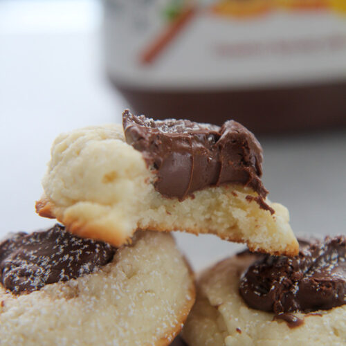 three nutella cookies with powdered sugar on top and a nutella jar in the background.