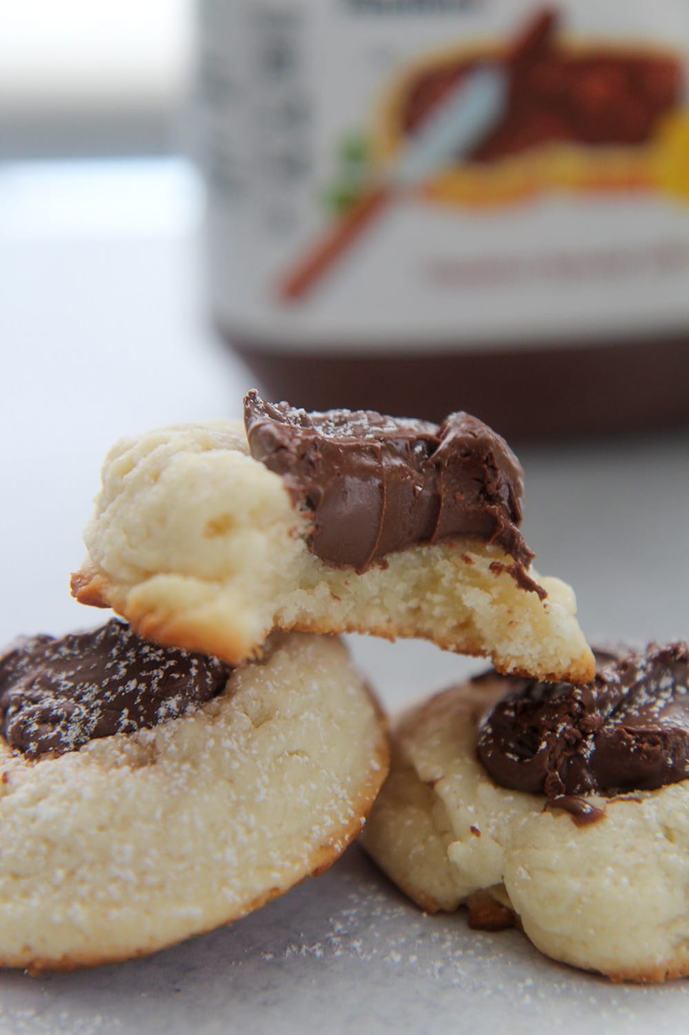 three nutella cookies with powdered sugar on top and a nutella jar in the background.
