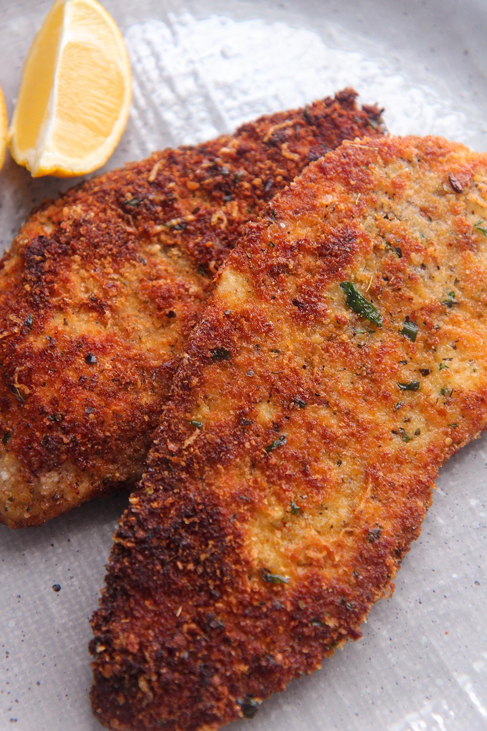 two crispy chicken cutlets with a lemon wedge on the side.