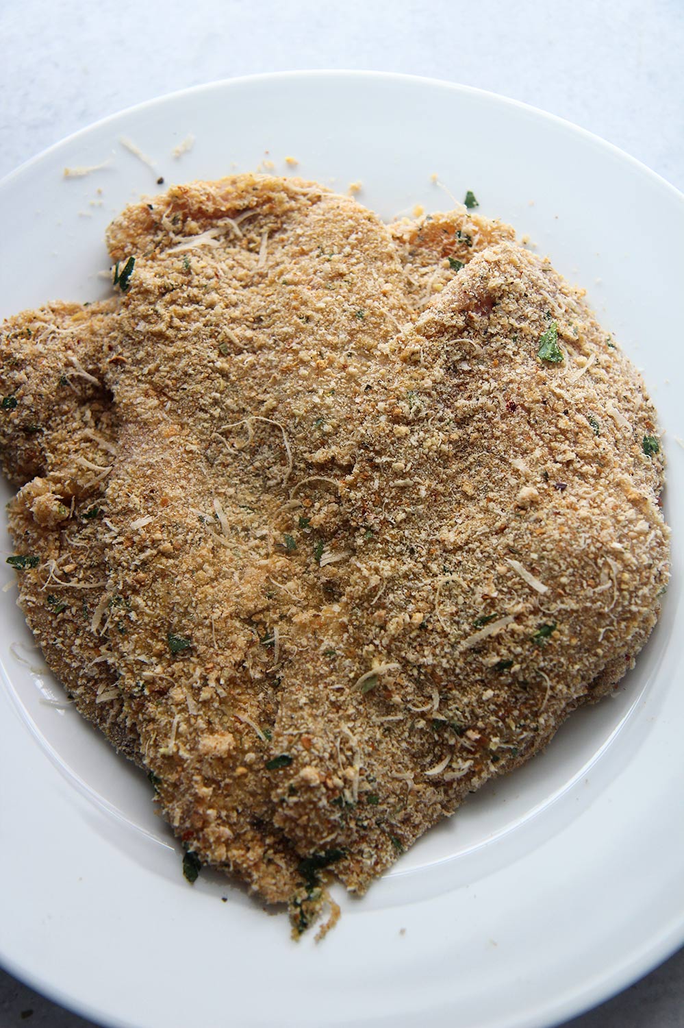 two breaded chicken breasts on a white plate.