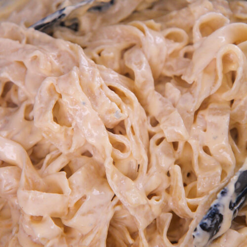 four cheese pasta in a skillet with tongs up close.