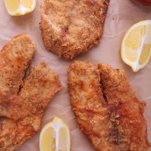 three fried tilapias on brown parchment paper.