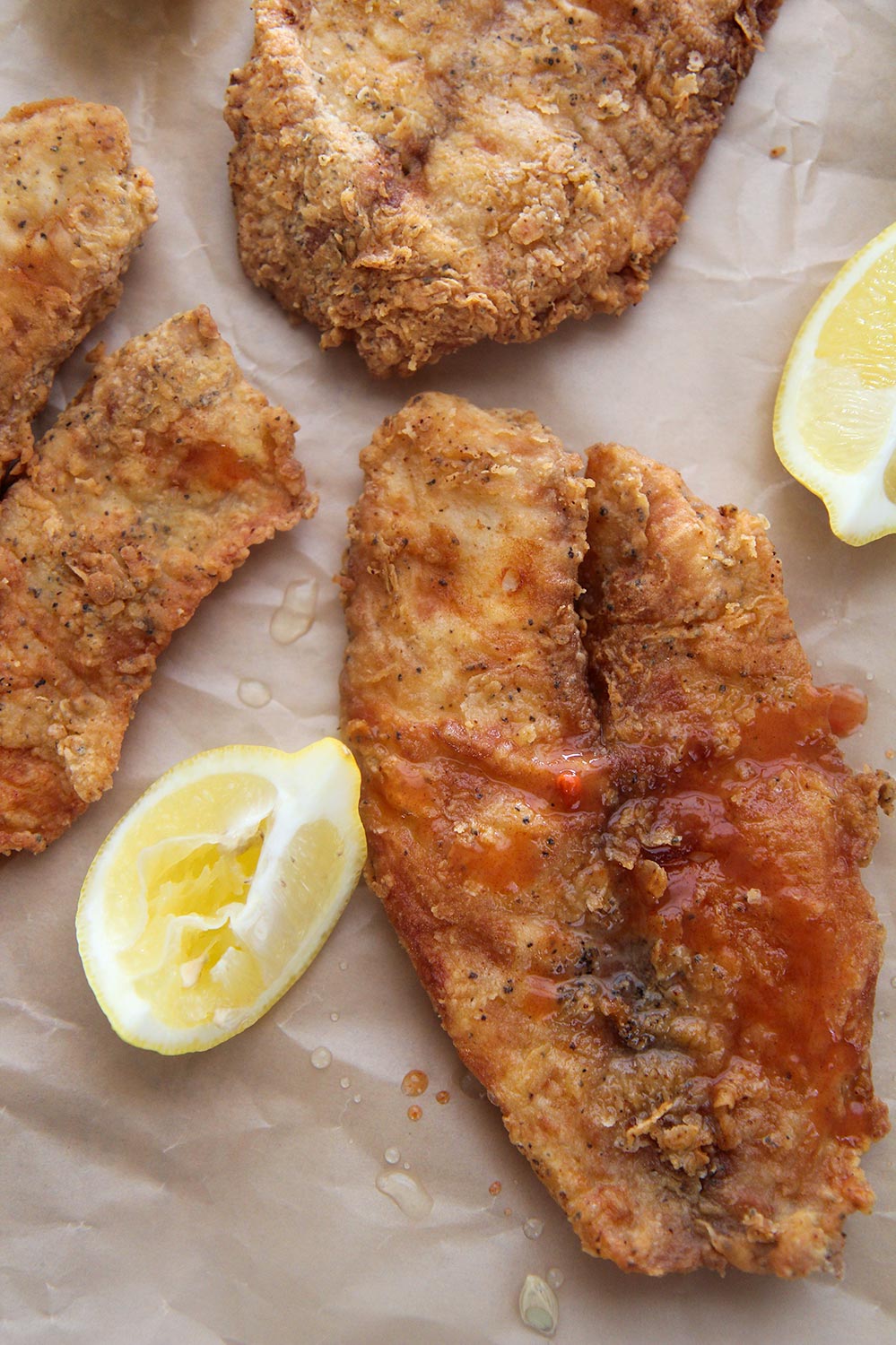 fried tilapia up close with lemon wedges on the side and hot sauce.