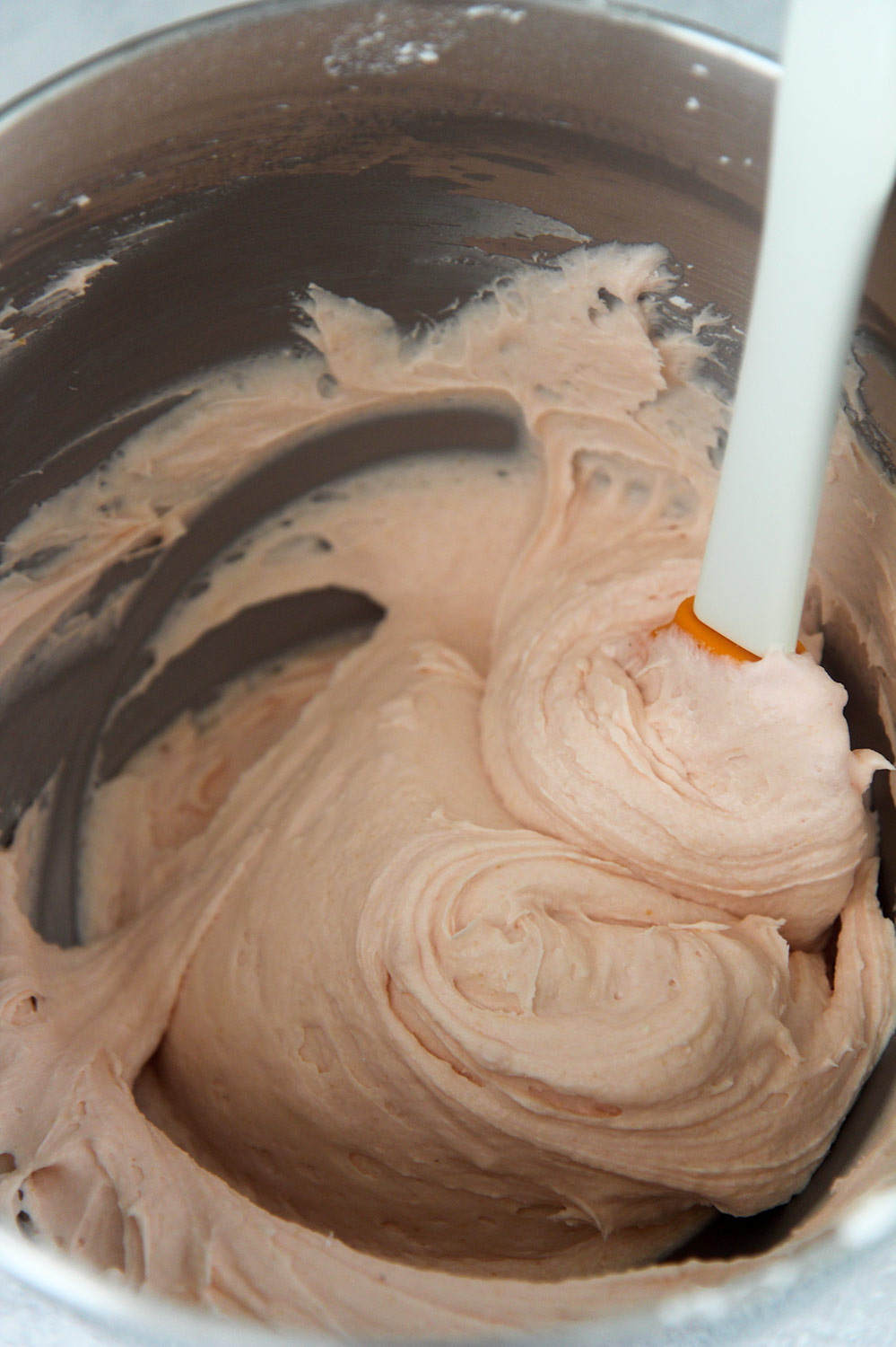 pink cream cheese frosting in a bowl with a spatula.