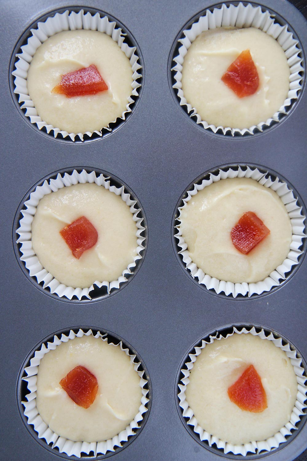 six cupcake liners filled with cupcake batter and guava paste.