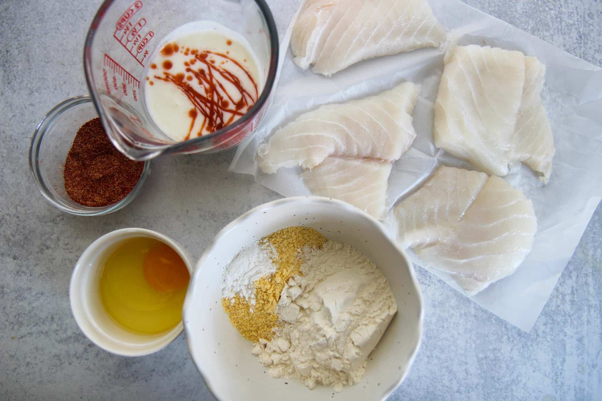 ingredients to make fried fish sandwiches, spices, egg, flour, cornmeal, cod, buttermilk, hot sauce, and baking powder. 