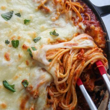baked spaghetti in a cast iron skillet with tongs.