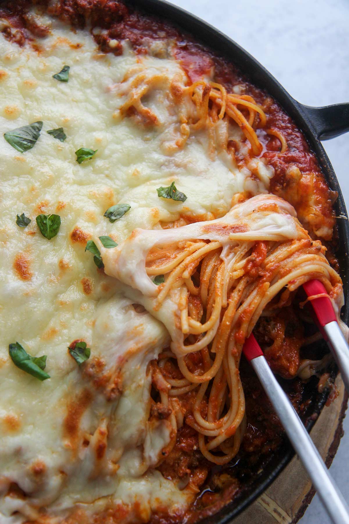 baked spaghetti in a cast iron skillet with red tongs.
