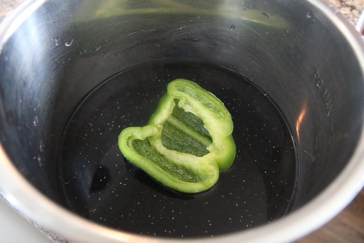 Black dried beans, water, and a green bell pepper in a pot. 