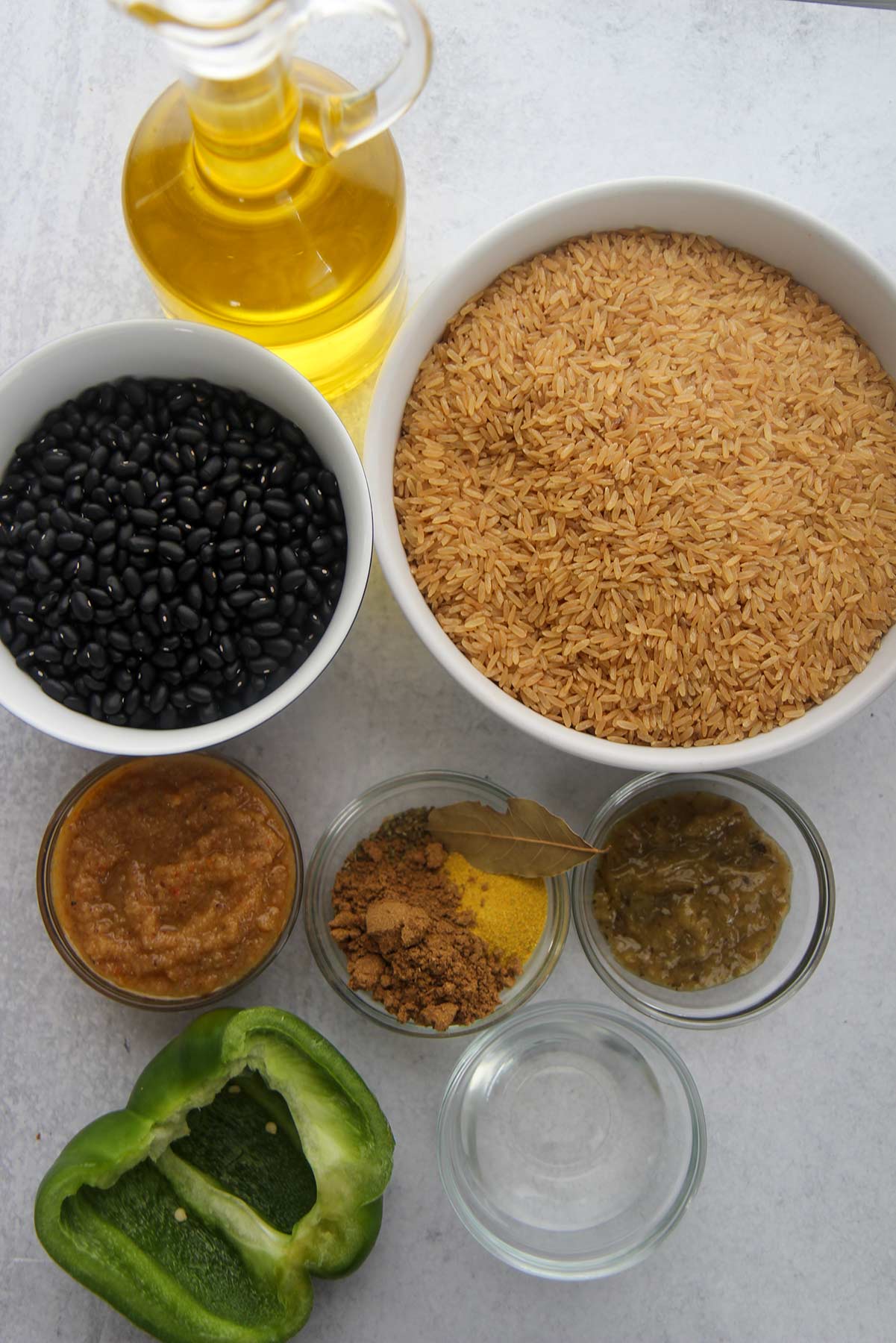 ingredients for congri, dried black beans, brown rice, small bowls with spices, vinegar, bay leaf, sofrito, and recaito. Oil and a green bell pepper. 