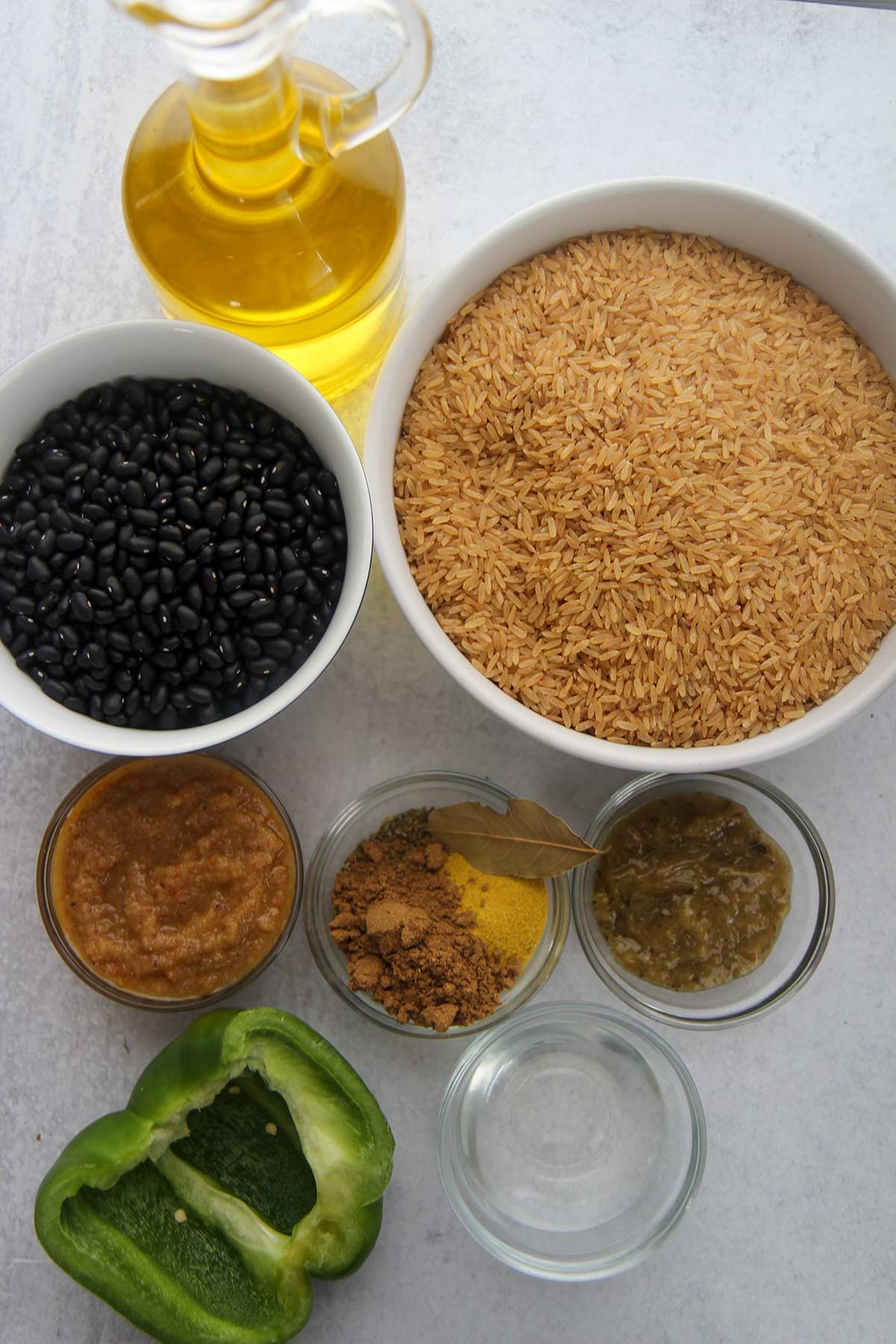 ingredients for congri, dried black beans, brown rice, small bowls with spices, vinegar, bay leaf, sofrito, and recaito. Oil and a green bell pepper.