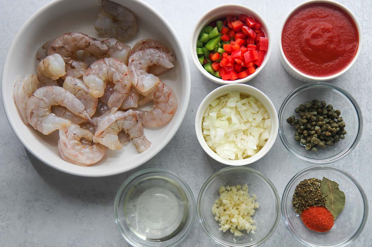 7 small bowls with ingredients and one large bowl with raw shrimp. 