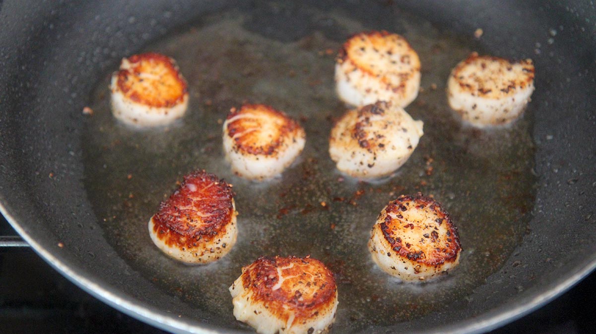 eight scallops cooking in a skillet on the stovetop. 