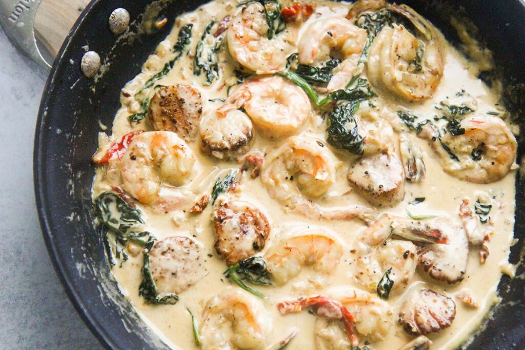 Tuscan shrimp and scallops with fresh spinach in a skillet. 