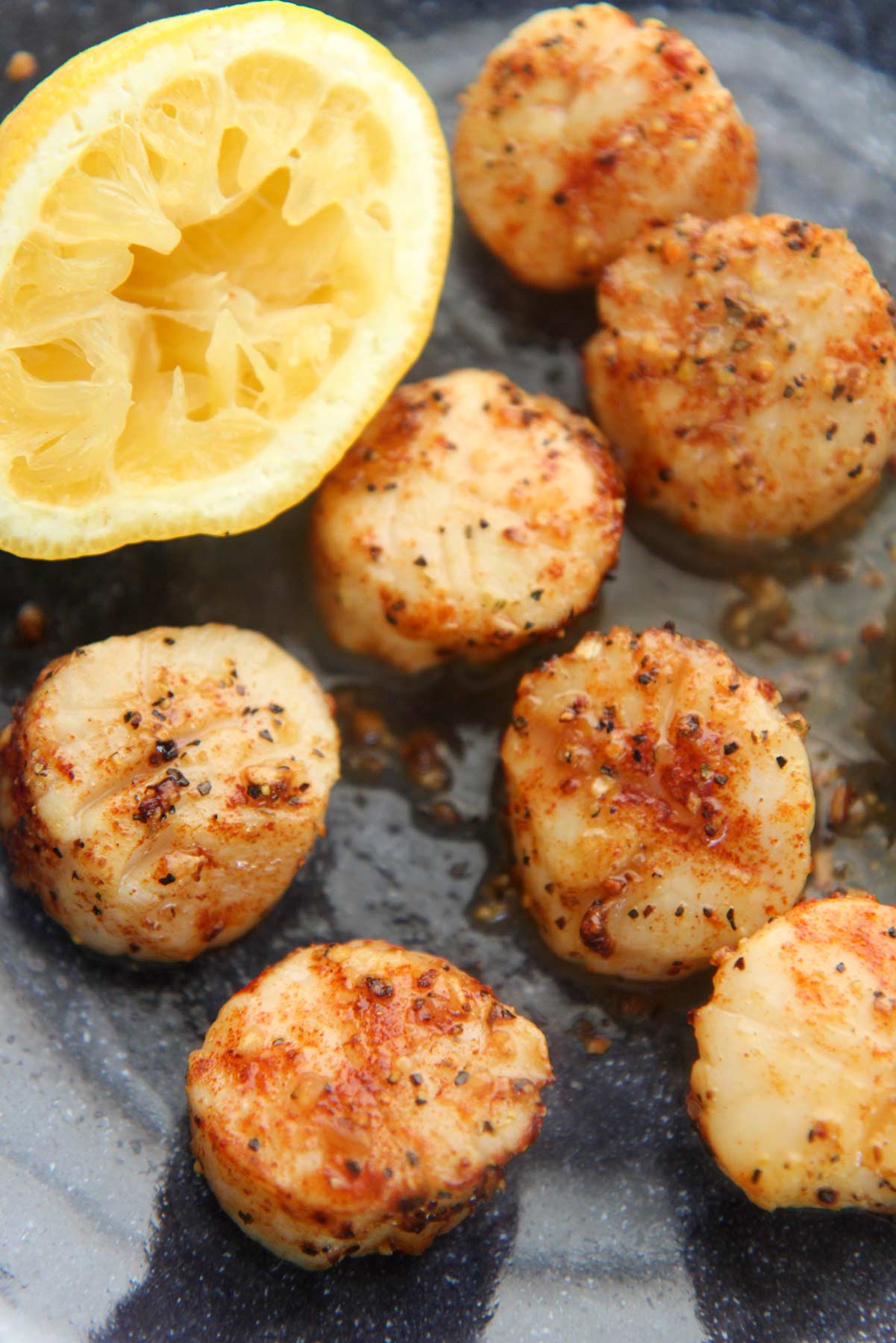 Seven air fryer scallops on a plate with a lemon on the side. 