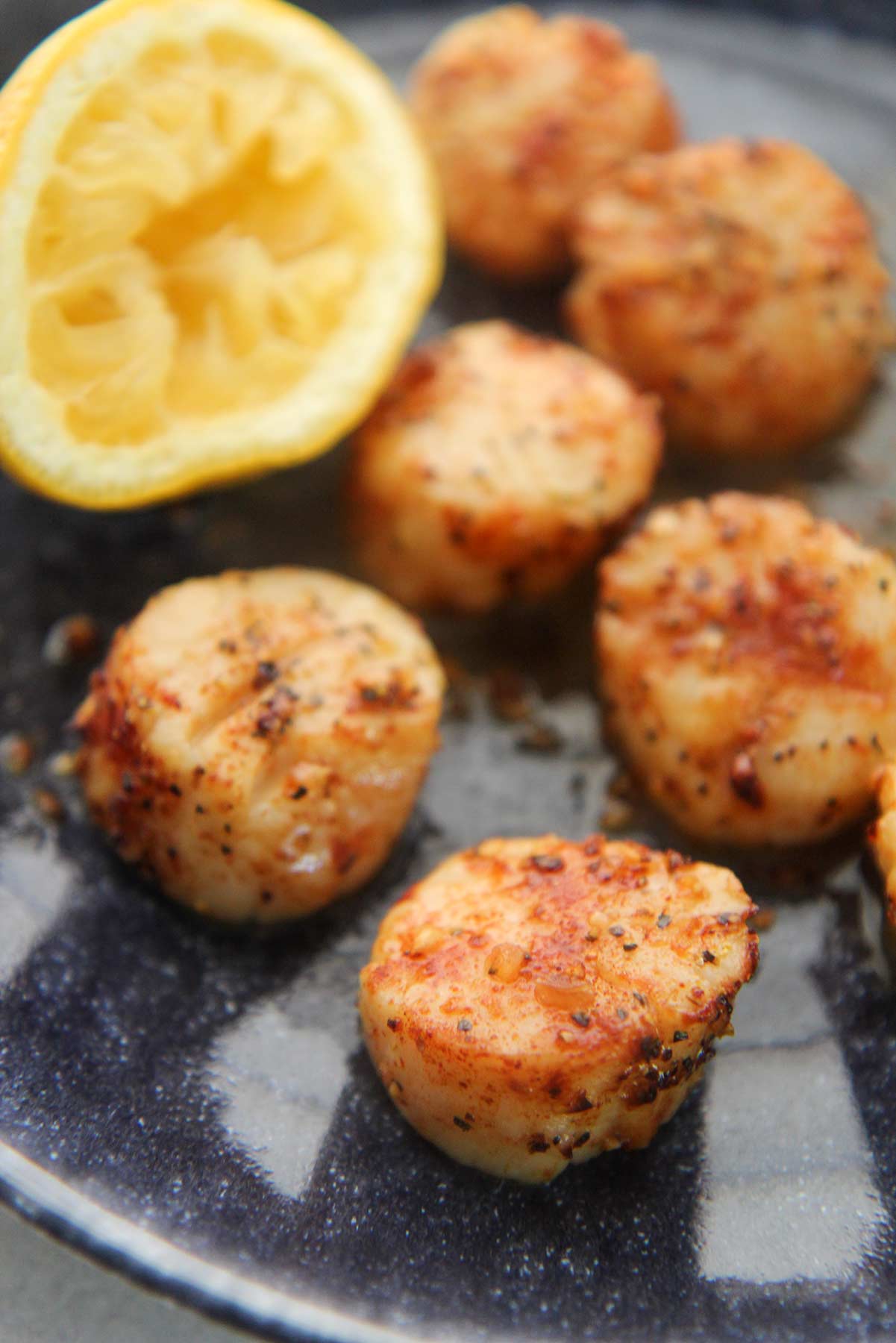 Cooked scallops on a plate with a lemon on the side. 