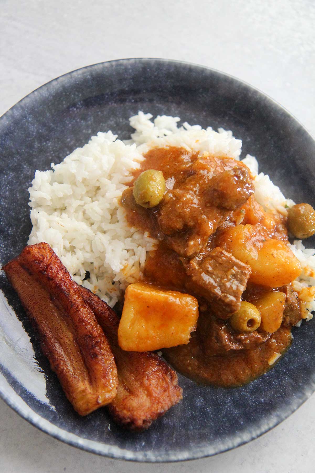 Carne guisada, white rice, and plantains on a plate. 