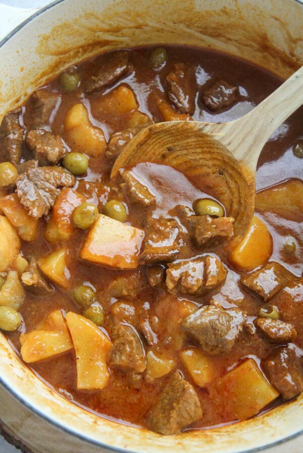 carne guisada de res in a large pot with a wooden spoon.