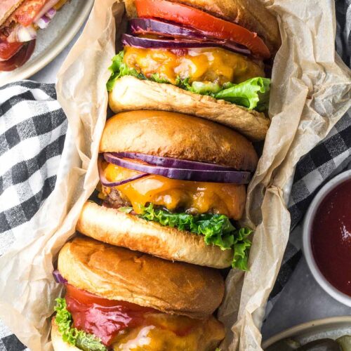 three cheeseburgers with lettuce, tomato, and onions.