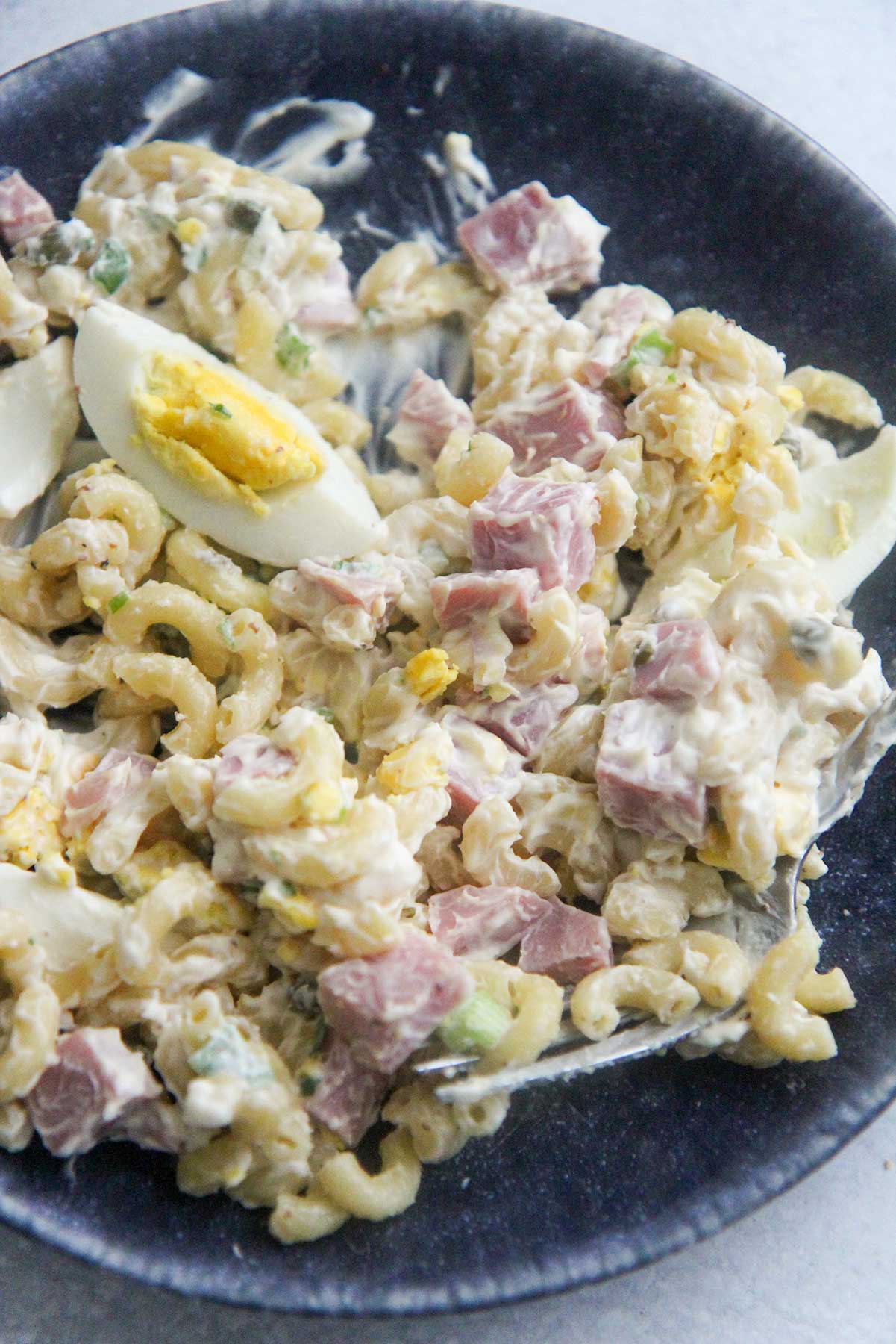 Macaroni salad with ham and eggs on a blue plate.