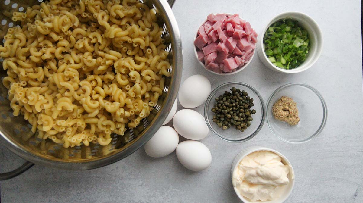 macaroni pasta, eggs, capers, ham, scallions, mayo and mustard in small bowls. 
