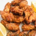 honey lemon pepper wings on a white plate with lemon wedges