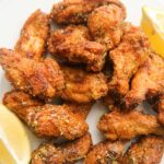 honey lemon pepper wings on a white plate with lemon wedges