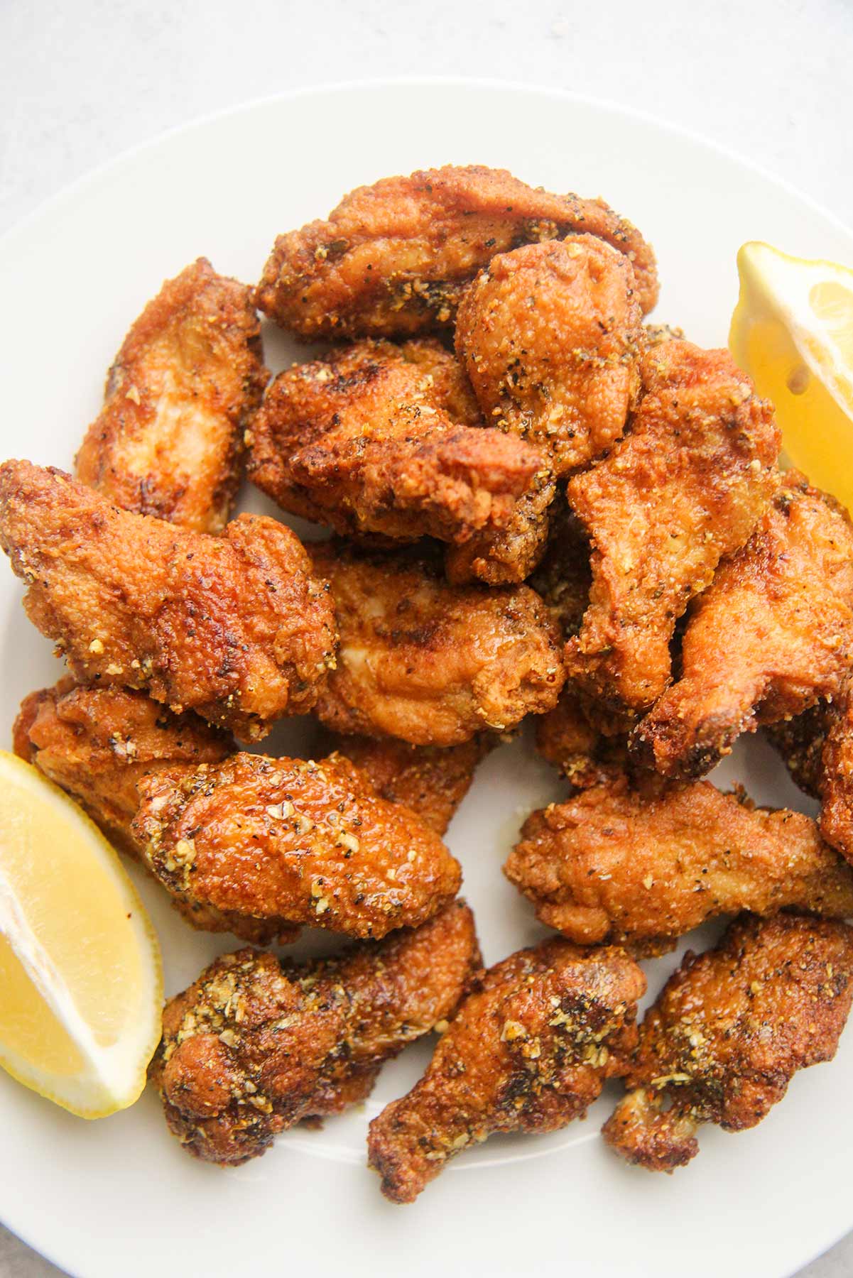 honey lemon pepper wings on a white plate with lemon wedges