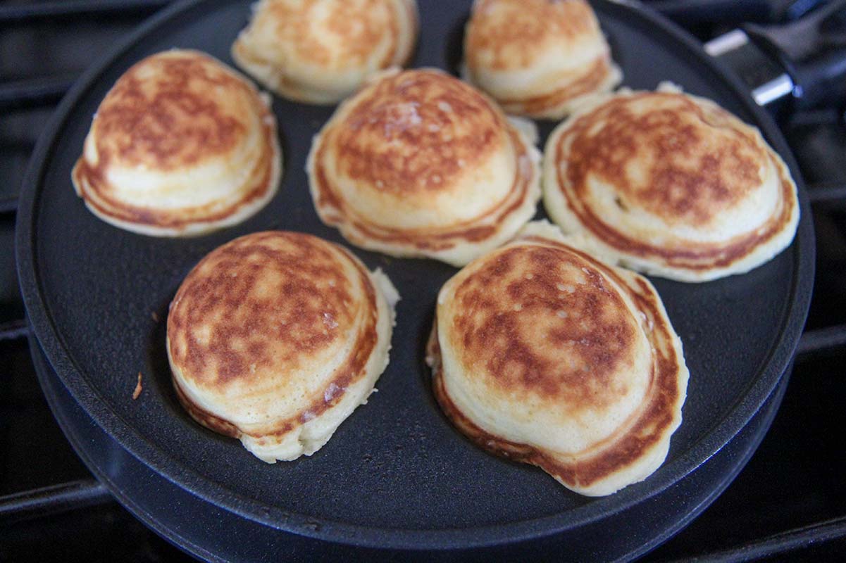 seven mini pancakes cooking in a pan. 