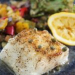 Chilean sea bass with vegetables, salad, and lemon.