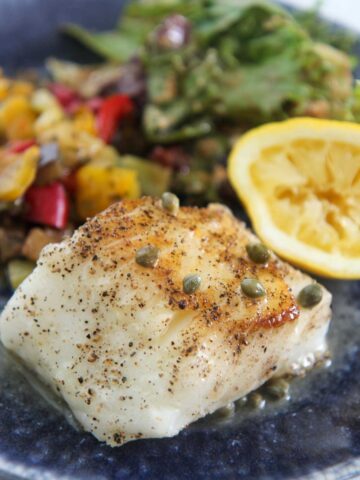 Chilean sea bass with vegetables, salad, and lemon.