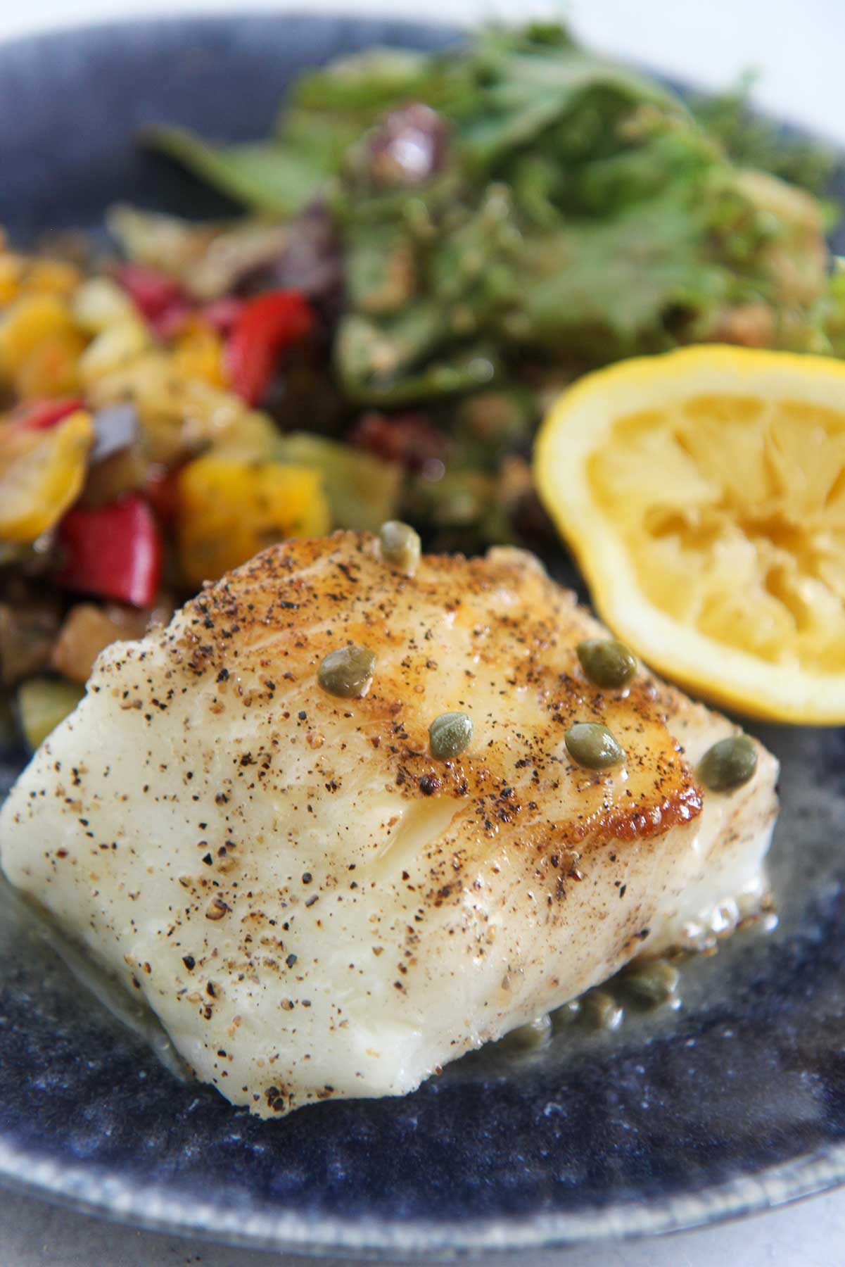 Pan-seared Chilean sea bass, salad, vegetables, and lemon on a blue plate. 